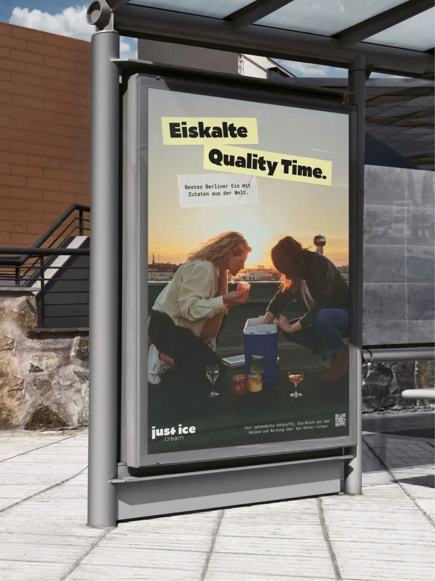 City-Light-Poster an einer Bushaltestelle: zwei Frauen hocken bei Sonnenuntergang auf einem Berliner Dach an einer Kühlbox mit Eisgläsern, Headline „Eiskalte Quality Time.“